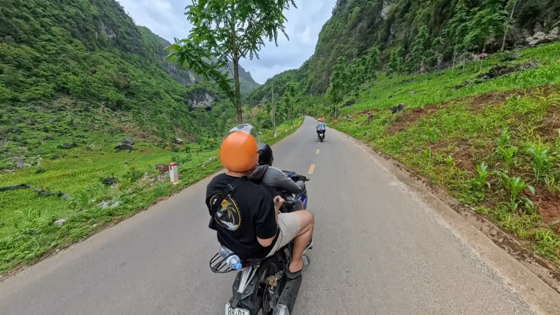 Two easy rider motorbikes on a paved Ha Giang Loop road with conical green karst mountains and farm fields, June 2026
