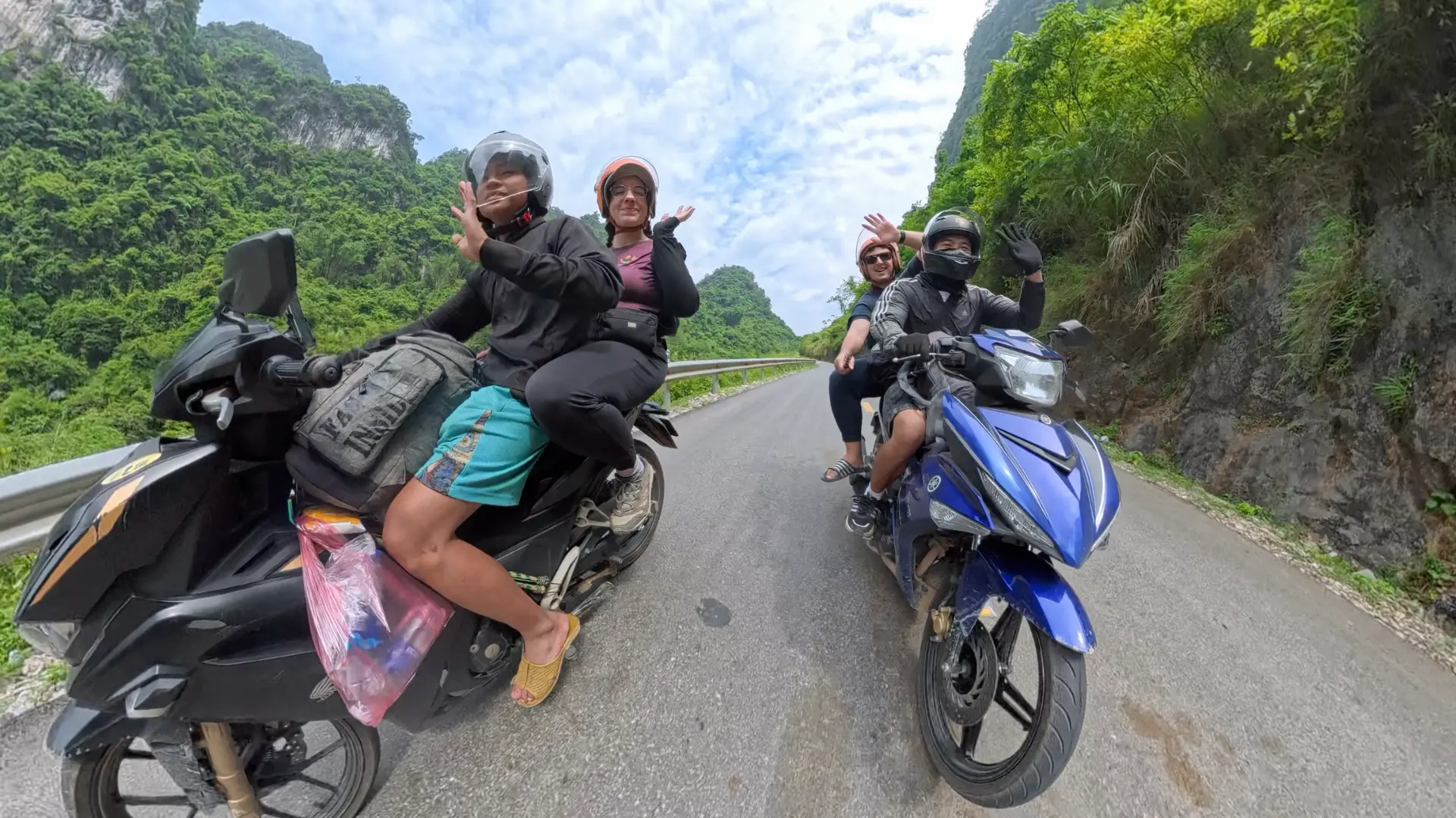 Two easy rider bikes with local drivers and travelers waving on a mountain road through green Ha Giang peaks, June 2026
