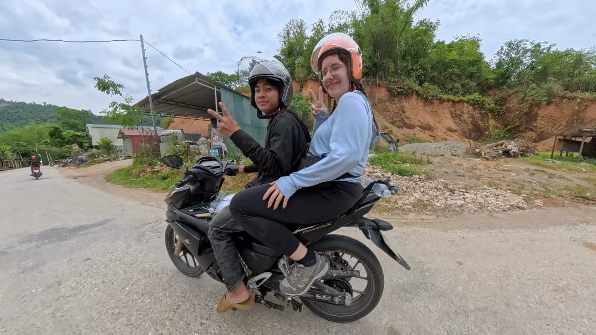 Easy rider passenger in an orange helmet on a paved Ha Giang Loop road through green karst mountains, photographed June 2026