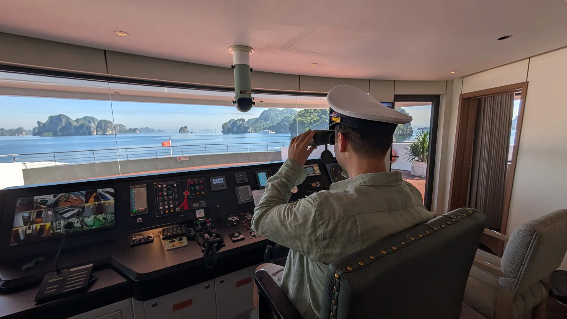 Liam in a captain's hat looking through binoculars from a cruise ship bridge over Ha Long Bay