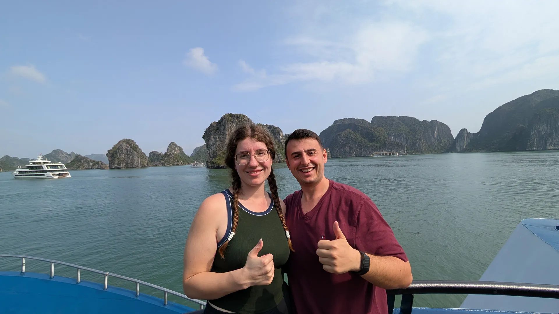 Liam and Sarah giving a thumbs up on a cruise sundeck with Ha Long Bay's limestone islands behind them