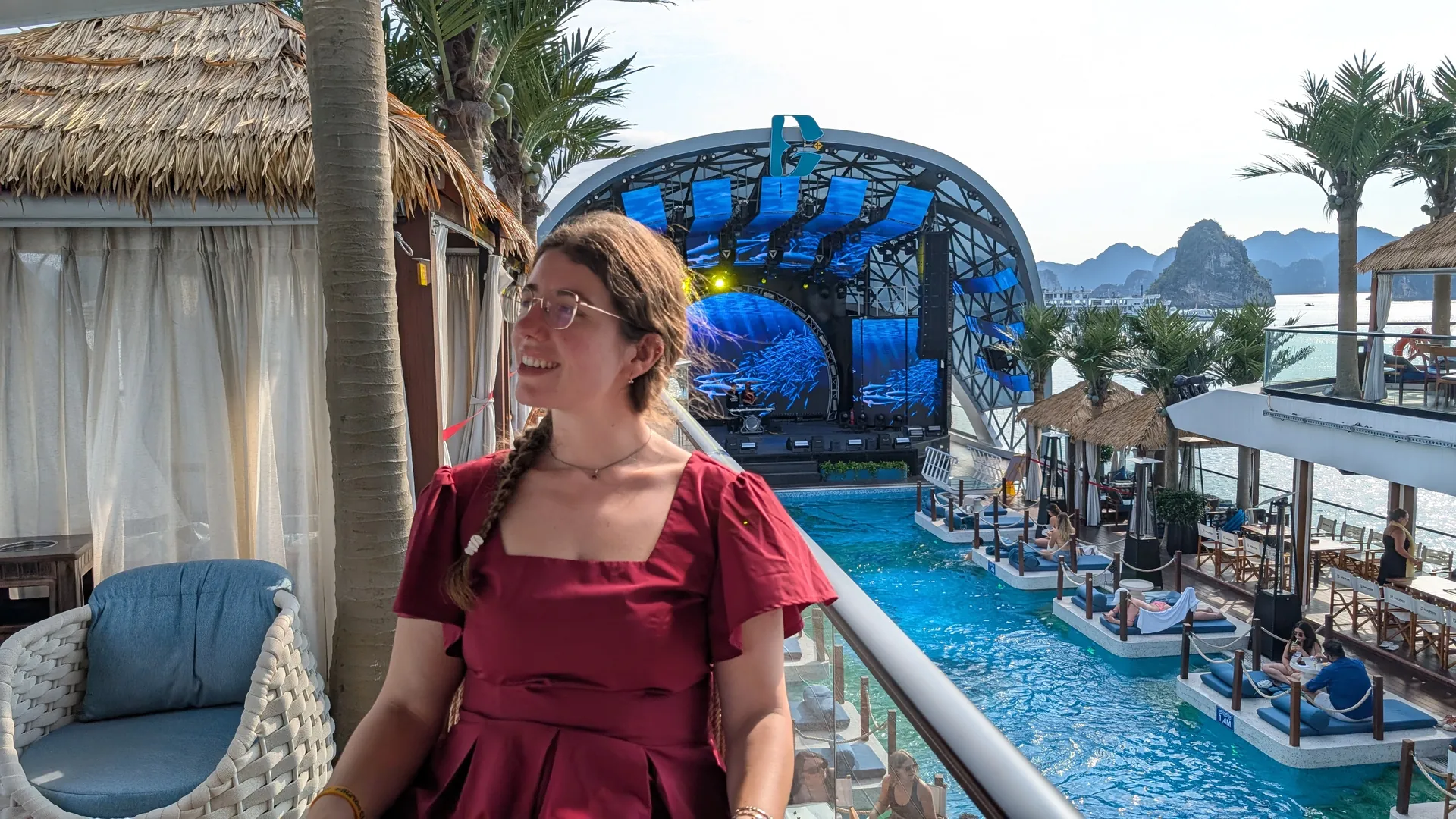 Sarah smiling on the Dolphin day cruise, with the pool deck, stage, and Ha Long Bay islands behind her