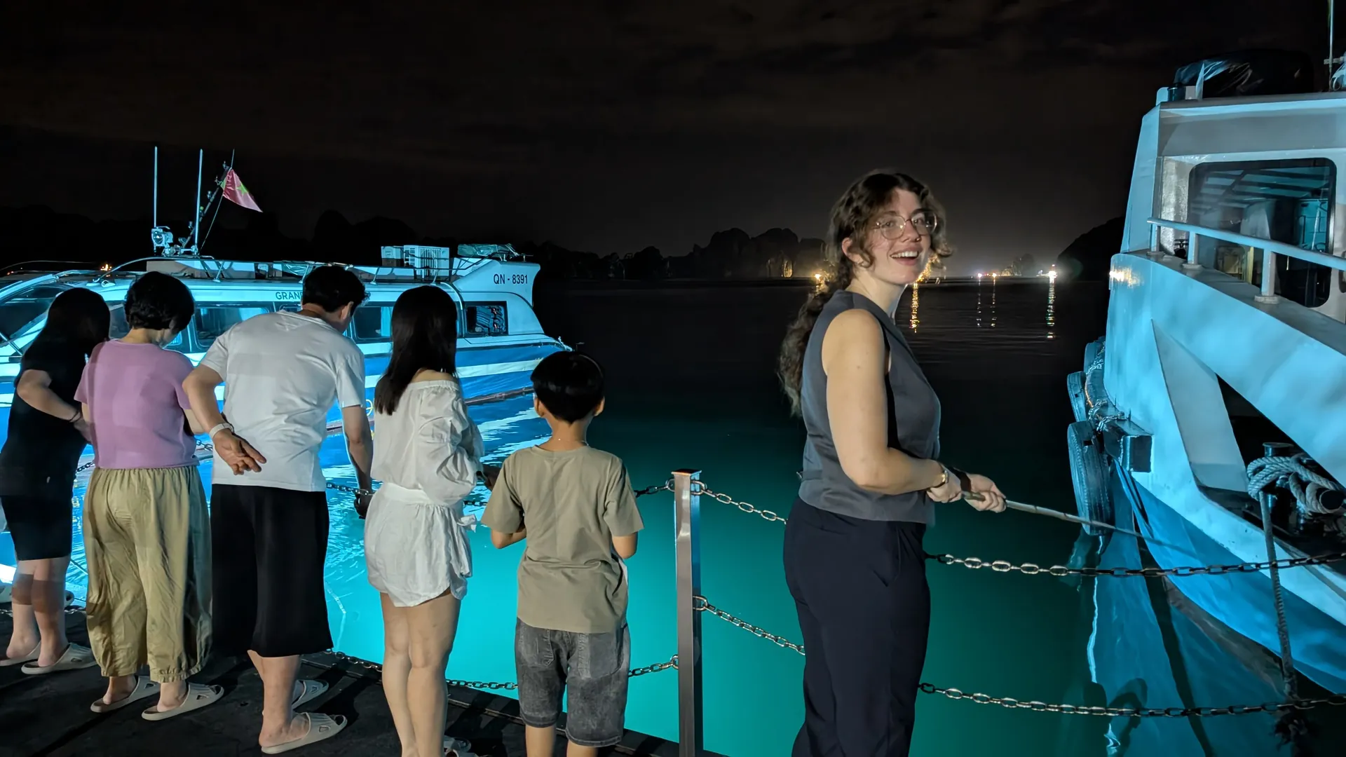 Sarah smiling on a lit pontoon at night while guests try squid fishing on a Ha Long Bay cruise