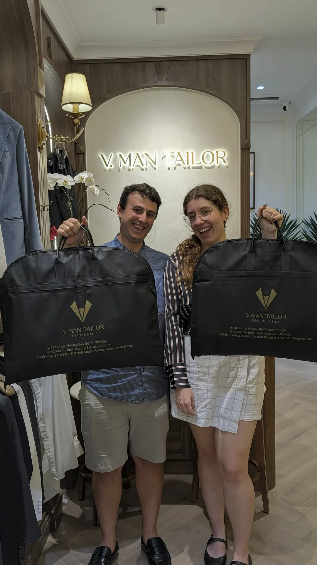 Liam and Sarah holding up their VMan Tailor suit bags in the shop