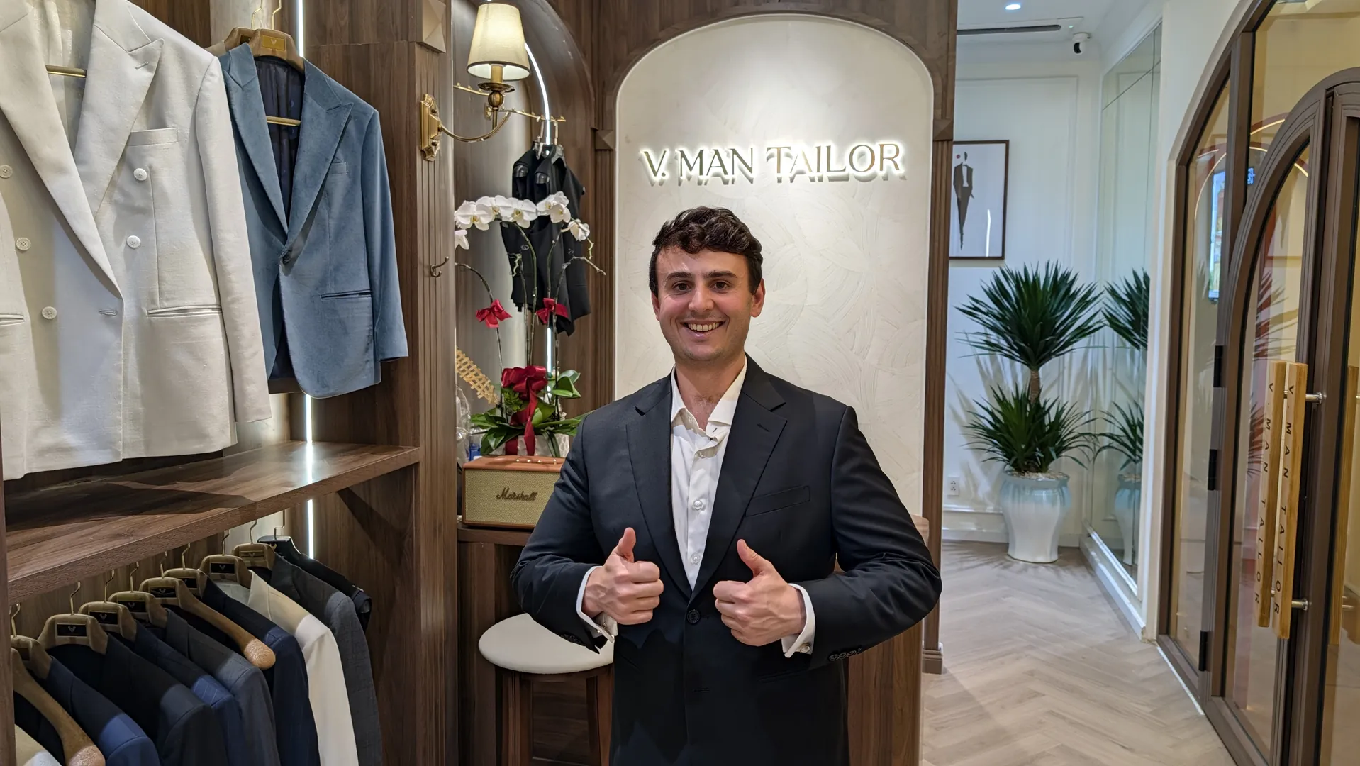 Liam giving two thumbs up in his black two-piece suit inside VMan Tailor