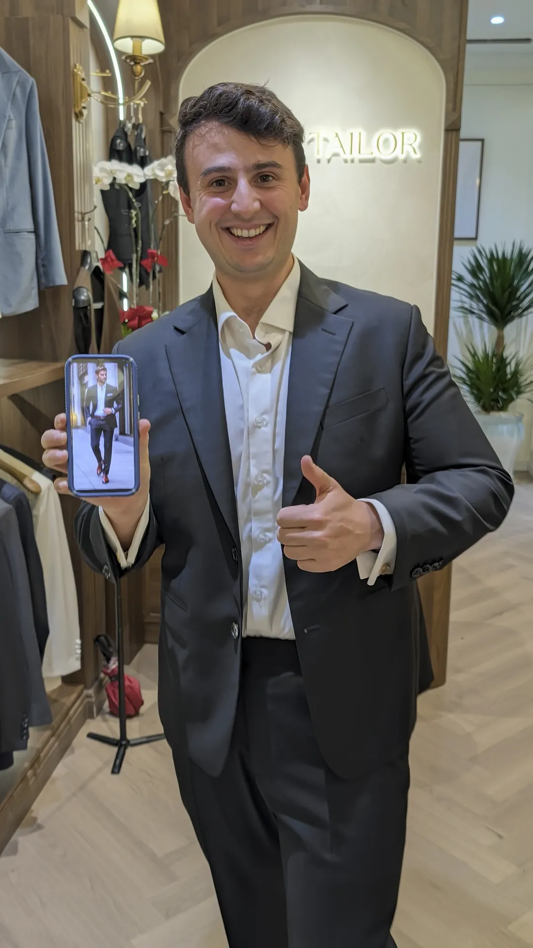 Liam in his finished black VMan suit holding up his inspo photo on his phone