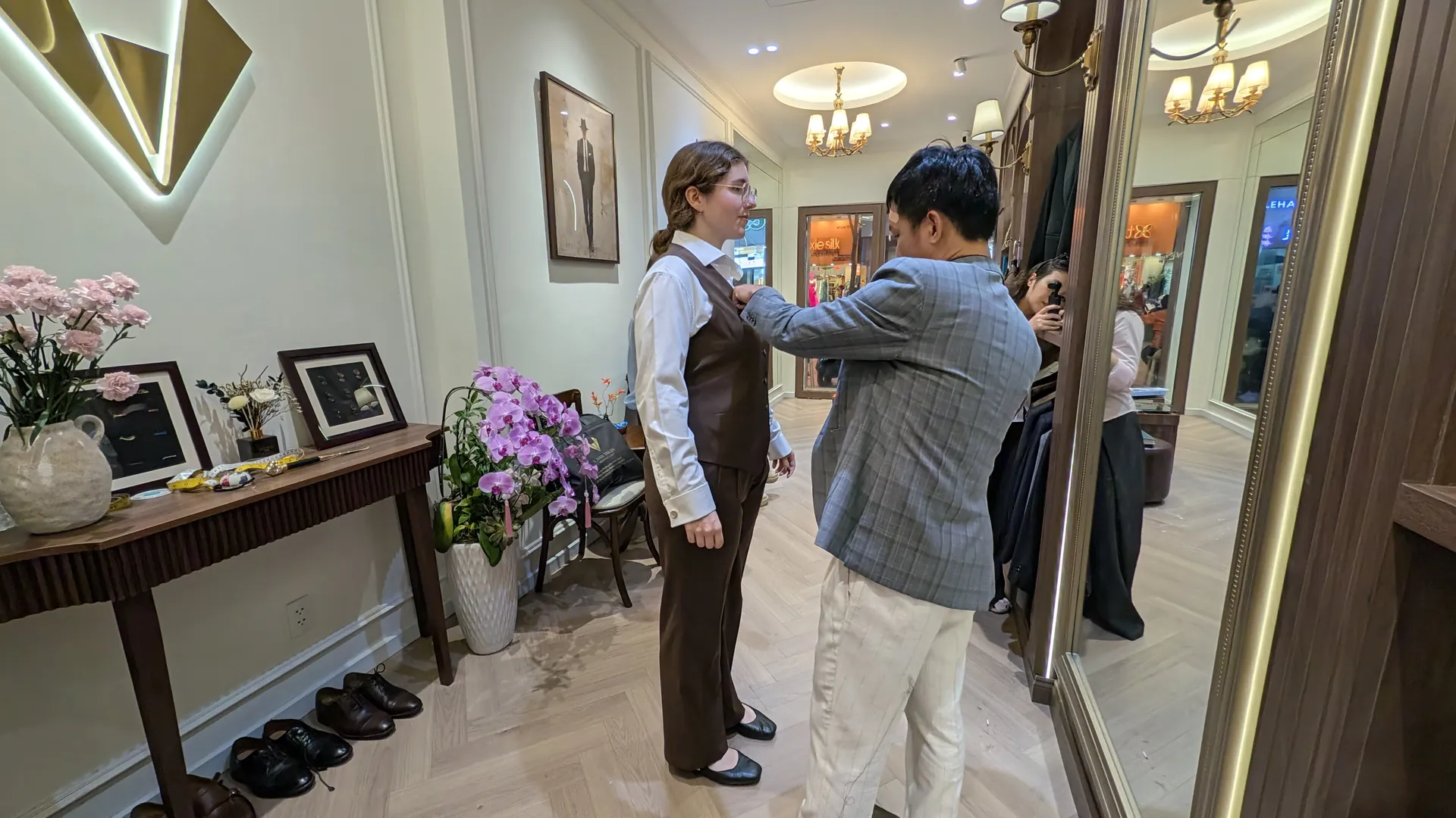 A VMan tailor adjusting Sarah's brown vest during a fitting