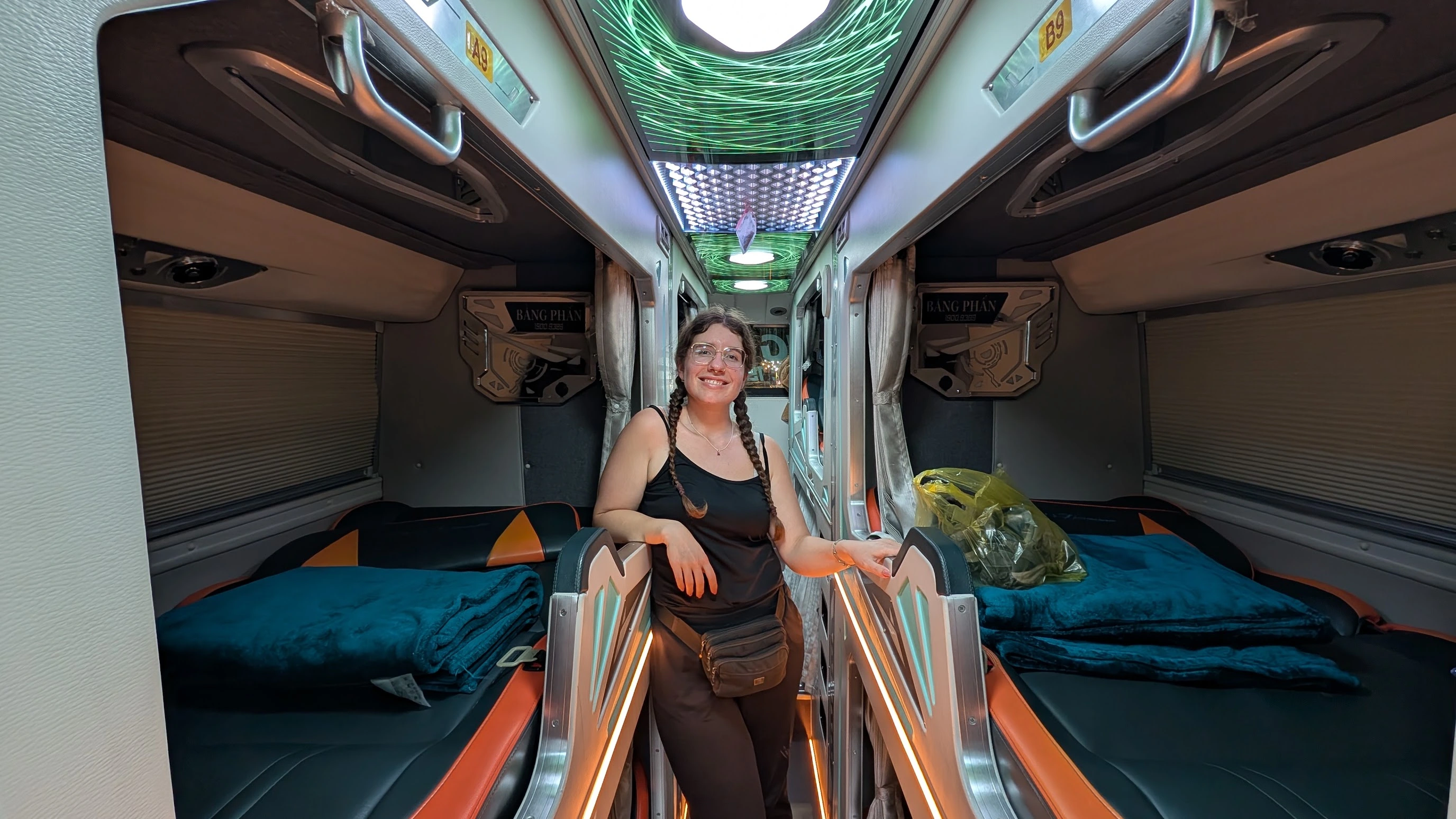 Sarah standing in the aisle of a cabin-style sleeper bus in Vietnam with private berths, mattresses, and curtains