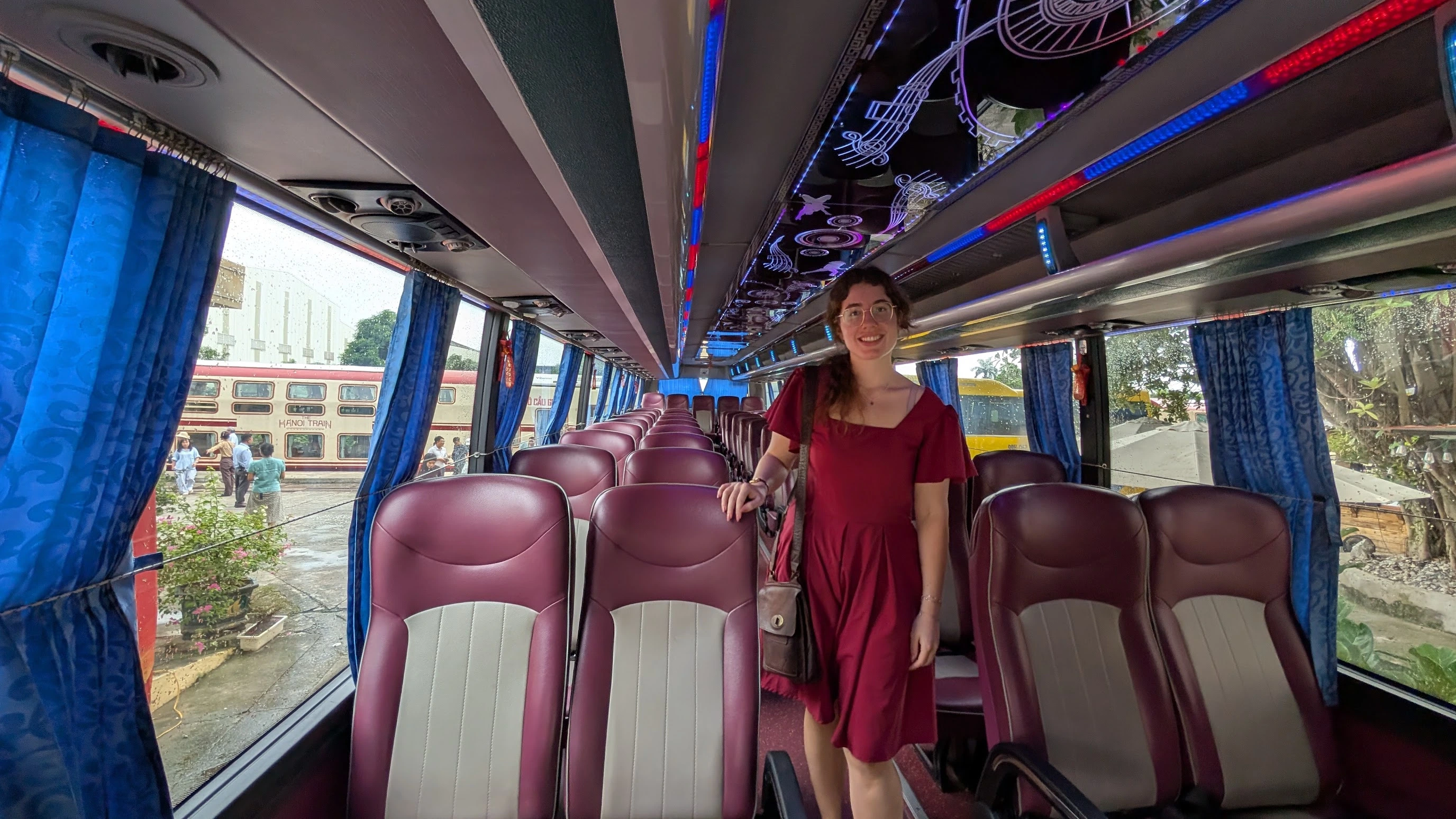 Sarah standing in the aisle of a modern tourist coach bus in Vietnam with LED ceiling lights and blue curtains