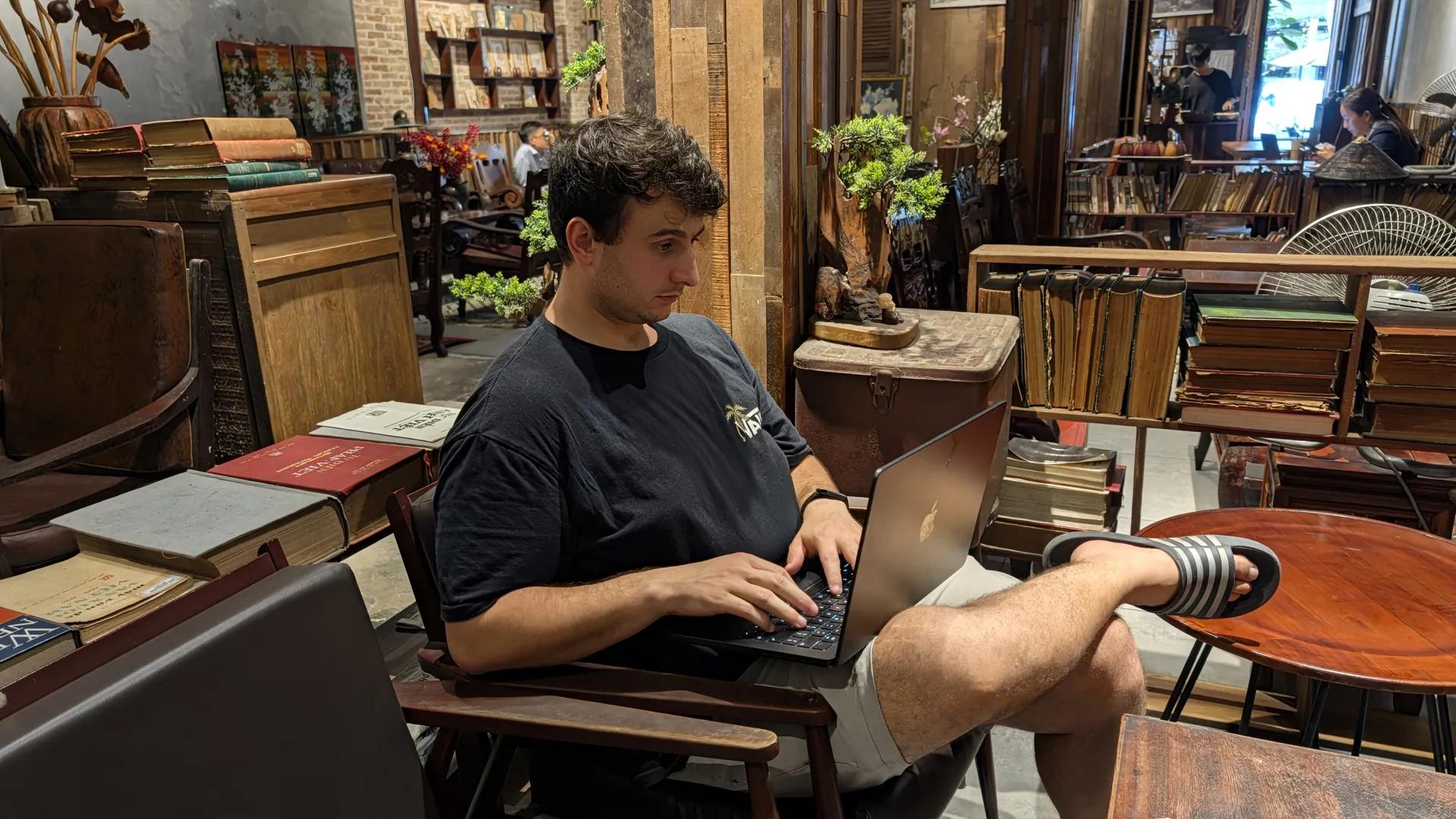 Liam working on a laptop with his legs crossed in a cafe, Vietnam, October 2026.