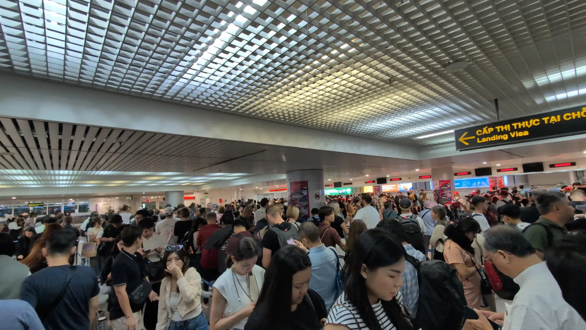 A packed crowd of arriving passengers waiting for immigration under the landing visa sign at Hanoi's Noi Bai airport