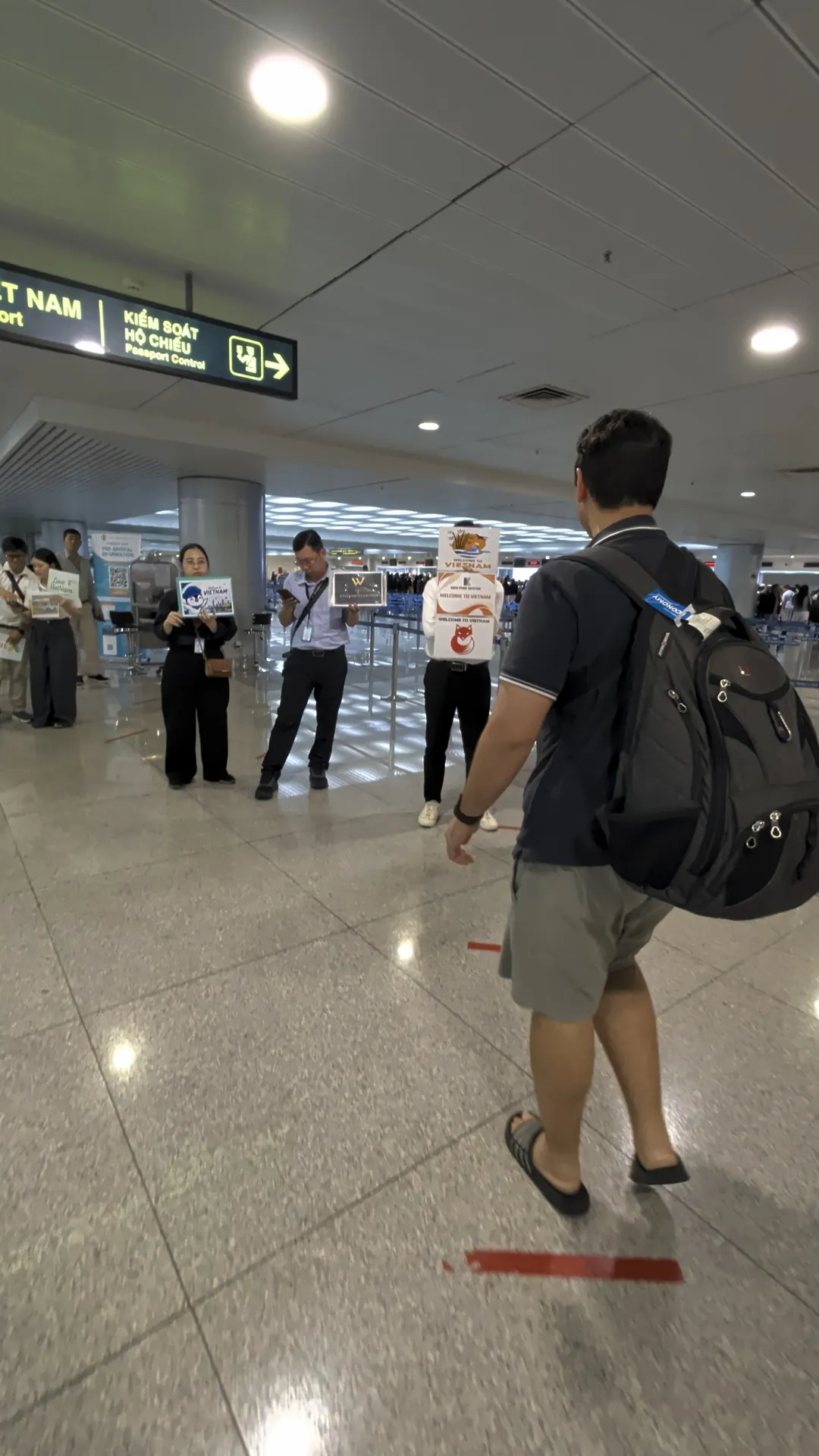 Liam with his backpack walking toward fast track staff holding signs near passport control in Ho Chi Minh City