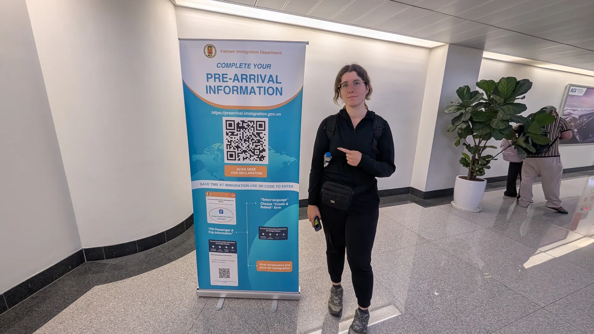 Sarah pointing at the Vietnam Immigration Department's pre-arrival information sign with a QR code at the airport