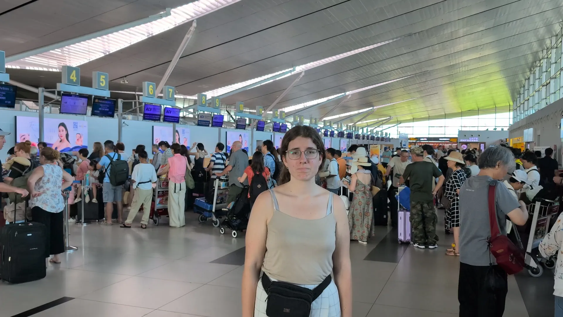 Sarah standing unimpressed in front of busy check-in counters at a Vietnam airport